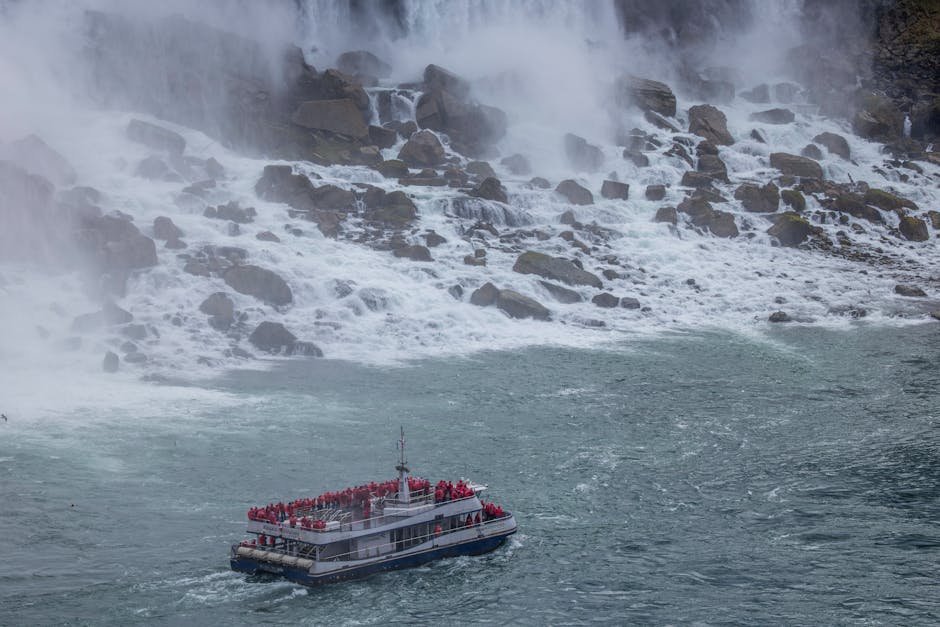 A tour boat filled with visitors in red ponchos approaches the base of a majestic waterfall at Niagara Falls.